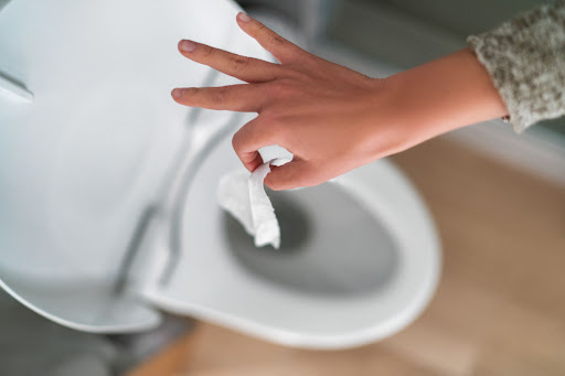 A hand holding a wet wipe over an open toilet.