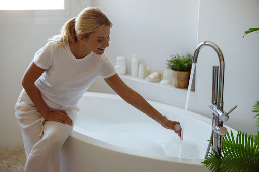 A smiling woman sitting on a tub that's running hot water.
