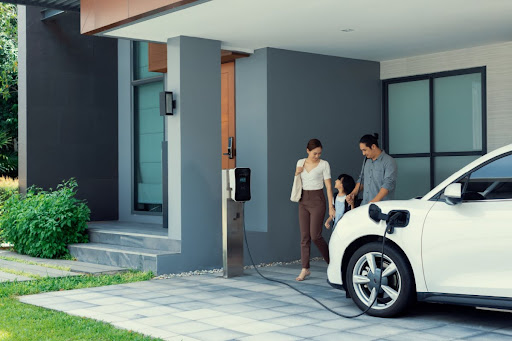 A family standing near an electric vehicle that is charging in a driveway.