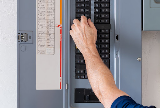 A close-up of a person's hand as they reach for a circuit breaker in an electrical panel.