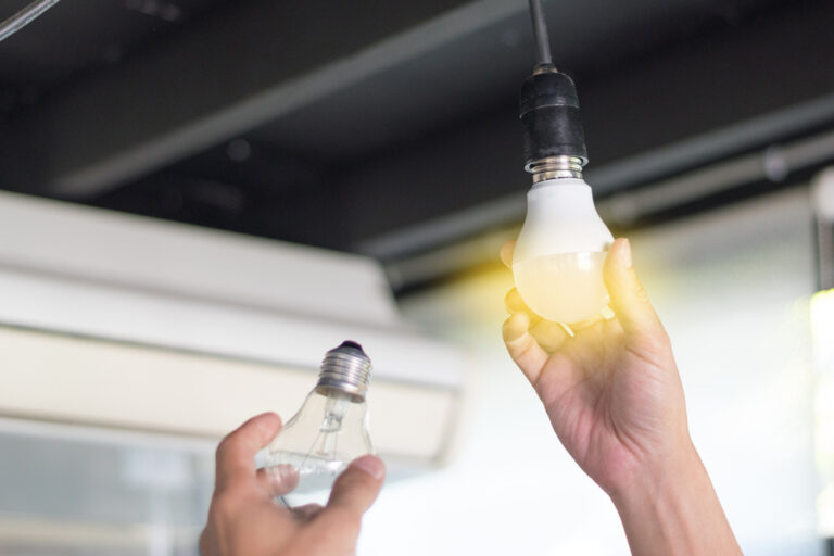 Homeowner installing LED light bulb in their home while holding old incandescent light bulbs to get rid of.