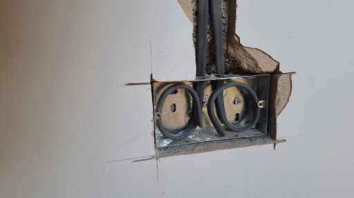 Hole cut into drywall to expose wires as part of a whole-home rewiring service.
